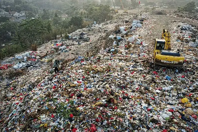 Overflowing waste landfill with construction debris and plastic waste, heavy machinery in action.